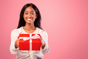 Holiday celebration. Portrait of black young woman holding wrapped gift box, giving it to camera on...