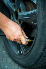 Man's hand inflating tire and checking air pressure with gauge pressure in service station 