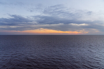 Golden sunset on the horizon, casting a serene atmosphere over the tranquil ocean waters and soft cloud formations in the sky