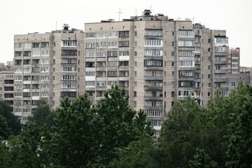 Large gray Soviet-style apartment buildings with balconies and antennas, partially obscured by lush...