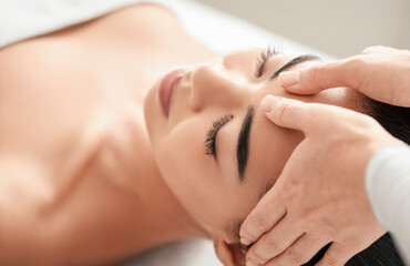 Spa therapist making relaxing head massage for beautiful asian woman, rubbing her forehead. Young female lying on table at beauty parlor with closed eyes, enjoying wellness treatments, closeup shot