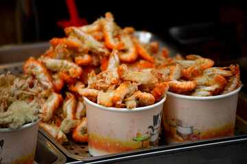 a large pile of deep-fried river shrimps in containers and on metal trays