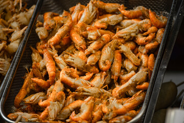 a large pile of deep-fried river shrimps in containers and on metal trays