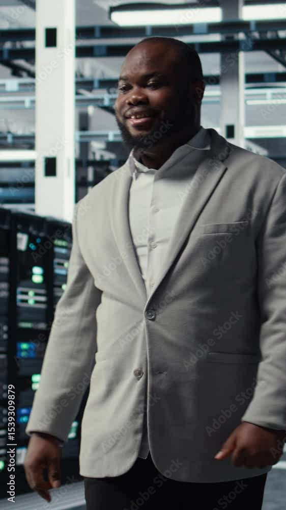 Poster vertical video smiling engineer walking in data center workplace with multiple rows of fully operati