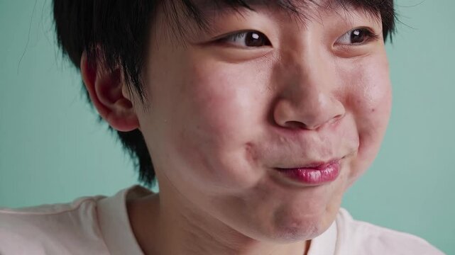 Playful Japanese Teen Boy Puffing Cheeks with a Cheeky Grin on Pastel Mint Background