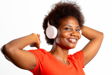 Young latin woman, with natural hair and wireless headphones, dances and smiles on white background