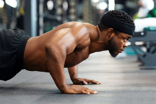Push-ups, press-ups workout. Muscular african american shirtless guy sportsman building up muscles, black man training on floor at modern gym, doing push-ups and looking at copy space, panorama - Powered by Adobe