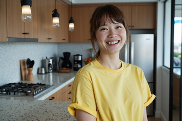 Happy young Asian woman standing in modern kitchen with bright smile, enjoying her contemporary home and relaxed casual lifestyle during pleasant day indoors
