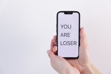 Cyber bullying. Woman holding smartphone with text You Are Loser on white background, closeup. Space for text