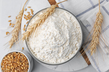 Wheat flour, grain and spikes on white table, flat lay