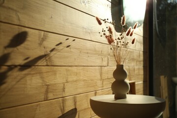 Dry flowers and spikes in vase on table near wooden wall indoors
