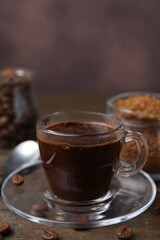 Cup of aromatic coffee, beans, instant powder and spices on wooden table, closeup