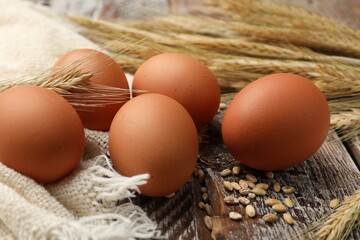 Raw eggs, fabric and spikes of wheat on wooden table, closeup