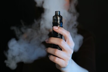 Woman using electronic smoking device on black background, closeup