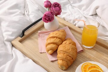 Tray with delicious breakfast and flowers on bed indoors, closeup