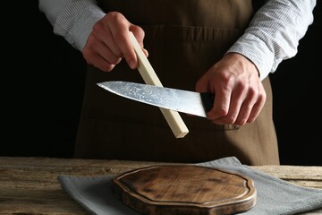 Man sharpening knife with sharpener on wooden table, closeup