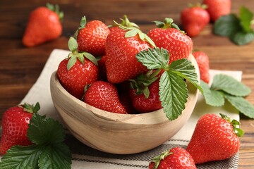 Fresh ripe strawberries and leaves in bowl on wooden table, closeup
