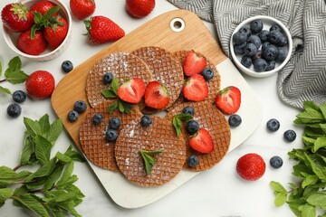 Tasty Dutch waffles (stroopwafels), mint and berries on white marble table, flat lay