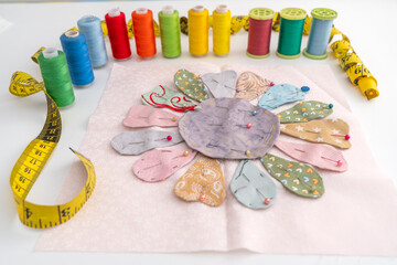 Ready to stitched flower applique quilt, yellow measuring tape and spools of multicolor threads;...