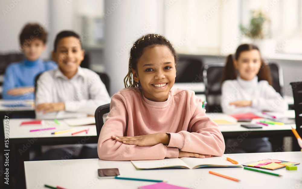 Poster elementary education. portrait of happy small african american girl sitting at table in classroom at