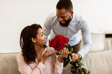 Making Surprise. Excited black girlfriend receiving bouquet of red roses from her happy boyfriend...