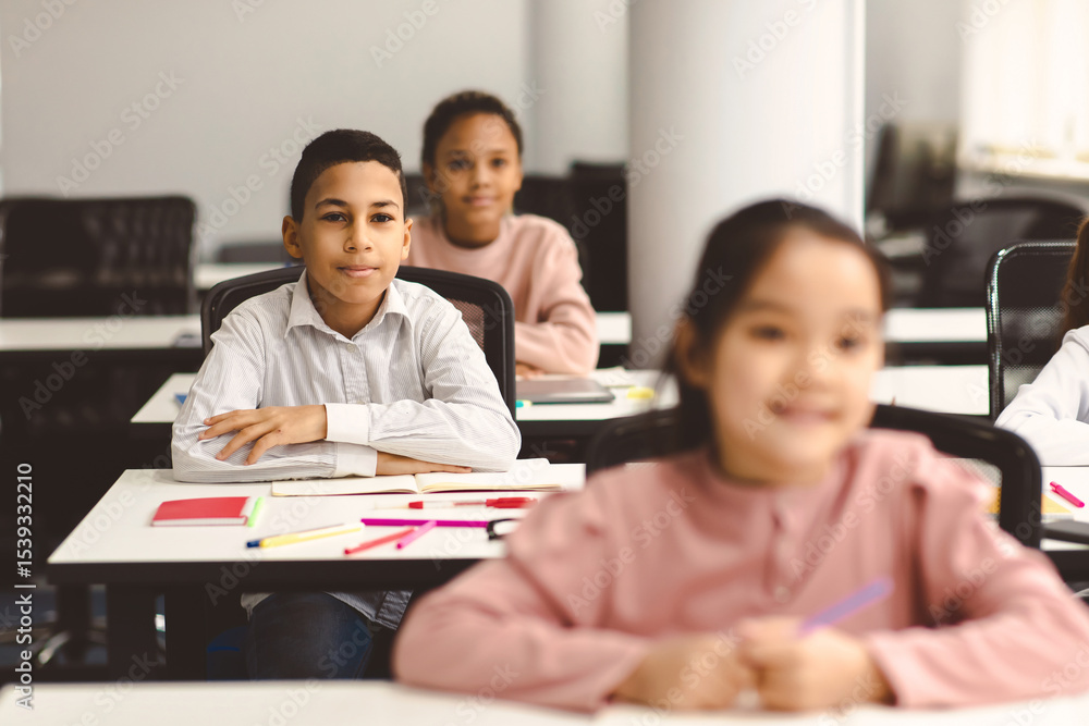 Poster elementary education. portrait of small smiling boy sitting at table in classroom at primary school 