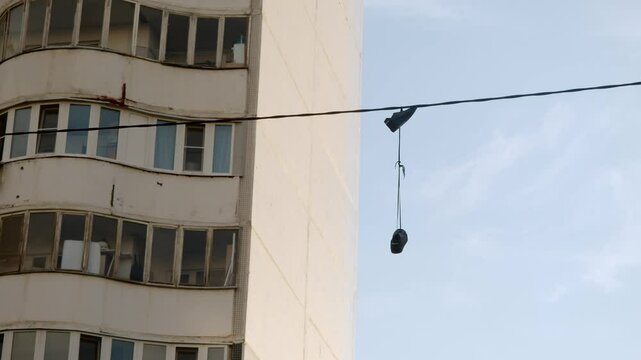 Black sneakers dangle from electrical wires in the cityscape. This is a place where gangs sell drugs. Shoe tossing. Wide shot