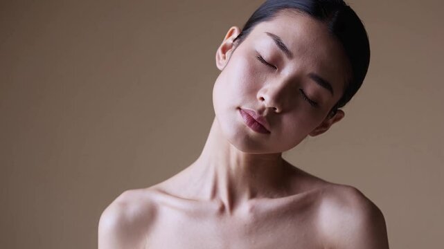 Japanese woman exhaling softly with relaxed shoulders and glowing skin under clamshell lighting against warm beige background