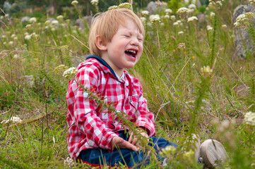 Little red-haired boy crying and sitting in grass field