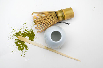 Traditional bamboo brush whisk with a spoon and matcha green tea powder splattered on white...