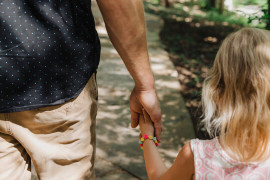 Close-up of father and daughter holding hands while walking outdoors, intimate parenting moment showing connection, trust, bonding, mindfulness, nurturing, childhood safety, and emotional support