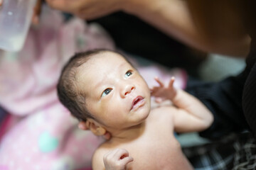A two-week-old Japanese baby lies wrapped in a pink blanket, held close in the arms of loving...