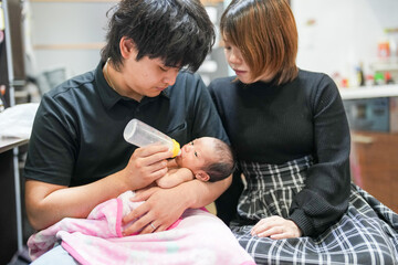 A two-week-old Japanese baby lies wrapped in a pink blanket, held close in the arms of loving...