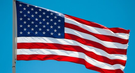 Fototapeta premium A flowing American flag against a bright blue sky, showcasing vivid red and white stripes with a blue canton filled with stars, highlighting patriotism.