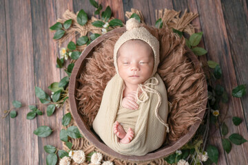 Professional newborn photo of a 2-week-old baby wrapped in a beige swaddle, sleeping in a brown...