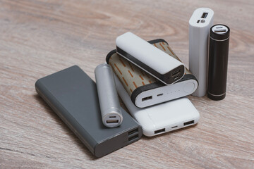 Assortment of portable power banks in various designs on a wooden surface. Portable chargers for gadgets.