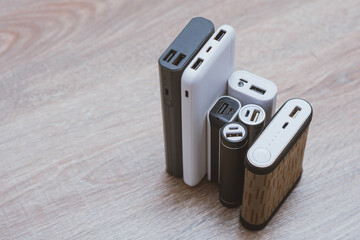 Assortment of portable power banks in various designs on a wooden surface. Portable chargers for gadgets.