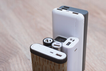 Assortment of portable power banks in various designs on a wooden surface. Portable chargers for gadgets.