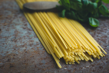 Close up of uncooked spaghetti pasta with basil leaves on a textured surface ready for cooking