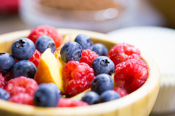 A wooden bowl filled with fresh blueberries raspberries and slices of peach on blurred background