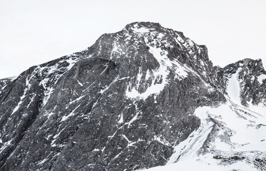 A majestic mountain peak covered in snow against a bright white sky on a cold winter day scene view
