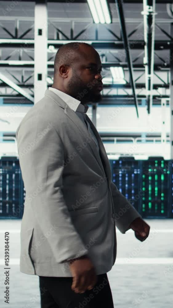 Poster vertical video system administrator walking in data center with rigs handling queries, doing backups