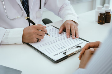 A doctor, wearing a white lab coat, holds a clipboard and pen, pointing towards it while...