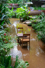Chairs and table submerged in flooded garden, surrounded by lush greenery and tropical plants