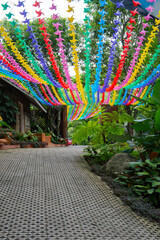 Colorful paper pinwheels hang above garden path, creating vibrant and festive atmosphere. path is lined with lush greenery