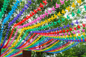 Colorful paper pinwheels hanging in rows create vibrant canopy against backdrop of green trees