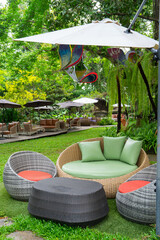 Outdoor seating area with wicker furniture and colorful cushions under umbrellas in lush garden setting