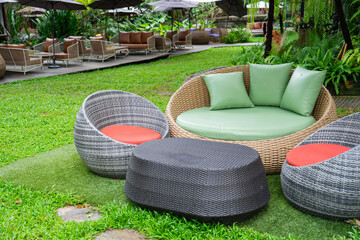 Outdoor wicker furniture set with green cushions on lush garden lawn, creating cozy and inviting atmosphere