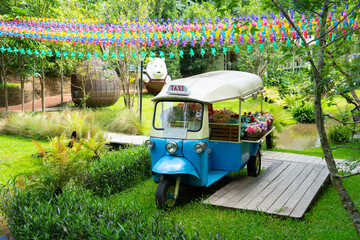 Colorful tuk tuk decorated with flowers sits in vibrant garden under canopy of multicolored ribbons