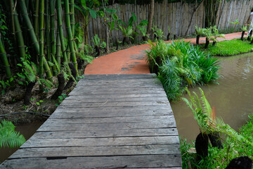 Wooden bridge leads to winding path surrounded by lush greenery and bamboo, creating serene garden atmosphere